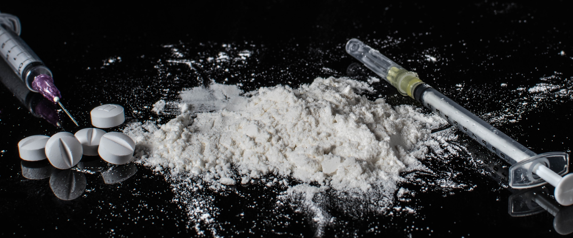 white powder, pills and syringes on a black background