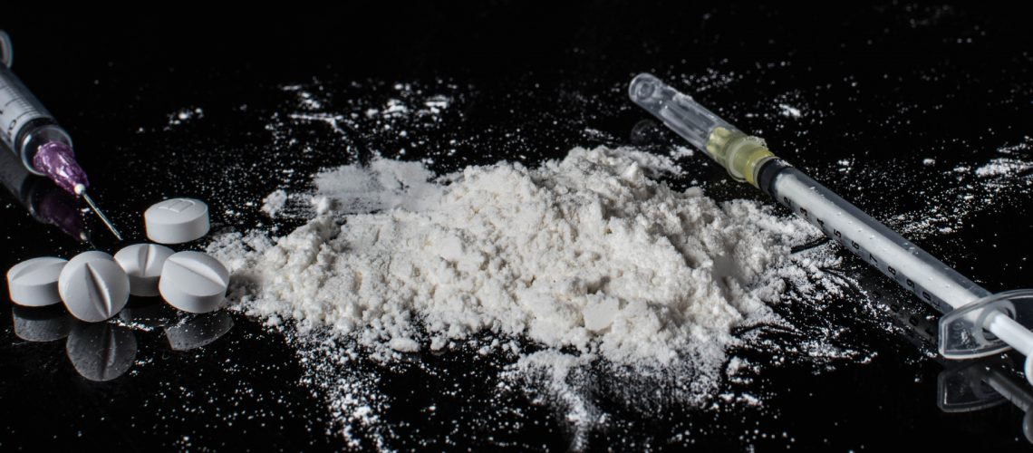 white powder, pills and syringes on a black background
