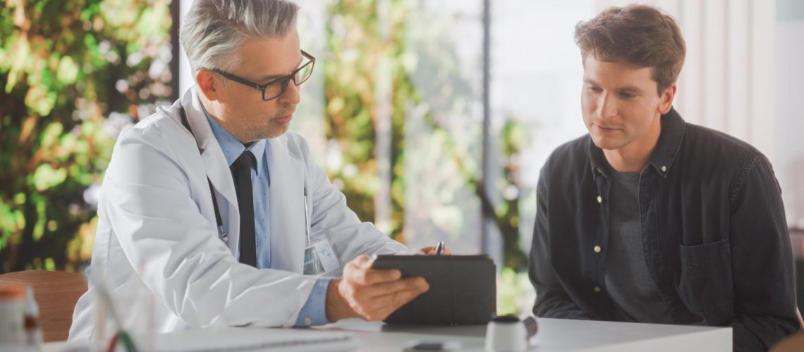 Male, older doctor holding a clipboard and explaining diagnosis to a younger male patient